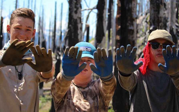Three young people wearing gloves show them to the camera during a service project with outward bound. 